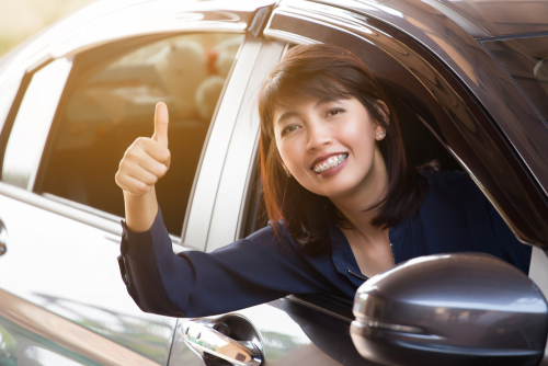 車の運転中に親指を立てる女性。