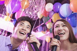 お祭りイベントで色とりどりの風船の前で歌う男女。