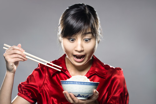 箸を持って丼一杯のご飯を持っている中国アジア系の若い女性。