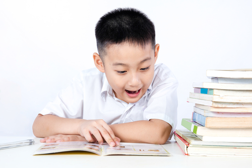 若い男の子が中国からの本の山の前で本を読んでいます。