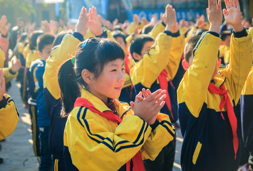 中国 黄色い制服を着た子供たちのグループが手を振っている。