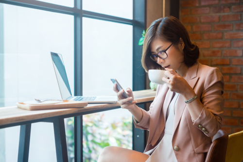 一杯のコーヒーと携帯電話を持ってテーブルに座っている中国の女性。