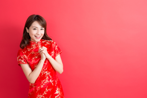 赤い背景にポーズをとるチャイナドレスを着た中国の女性。