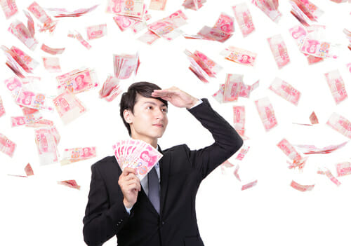 中国でスーツを着た男性が空から降ってくるお金を眺めている。