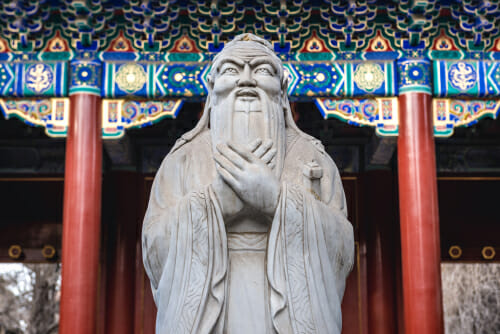 華美な建物の前に立つ中国人男性の銅像。