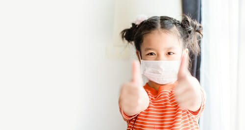 中国で手術用マスクをかぶって親指を立てる少女。