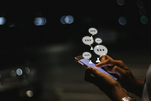 中国で、夜にチャットバブルが表示された携帯電話を使用している人。