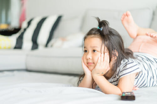 リモコンを持ってソファに横たわる中国の小さな女の子。