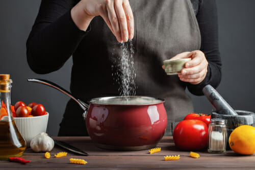 女性が中華鍋の野菜に塩をまぶしている。