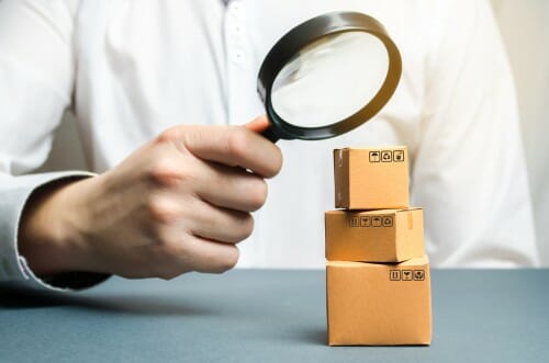 中国で男性が虫眼鏡で山積みの箱を調べている。