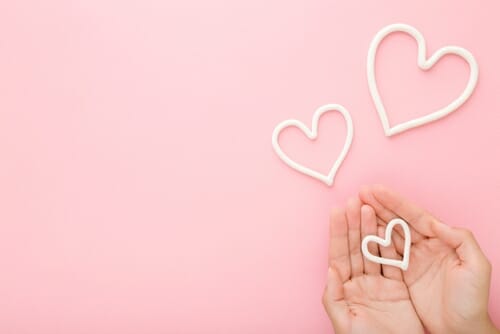 中国のピンクの背景にハートの形を持つ女性の手。