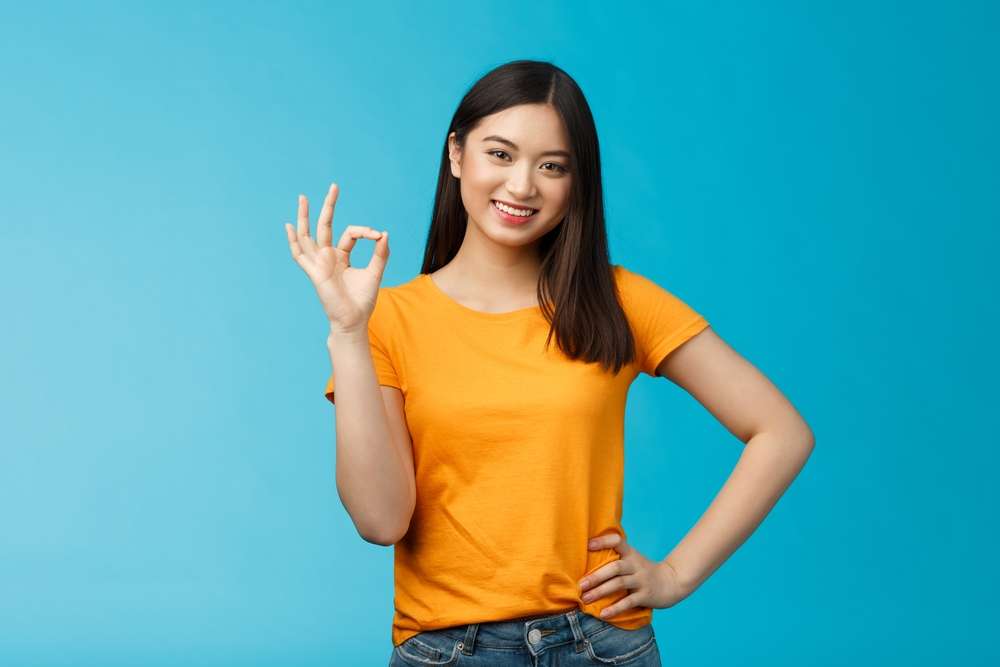 青い背景にOKサインを表示するアジア系の若い女性。