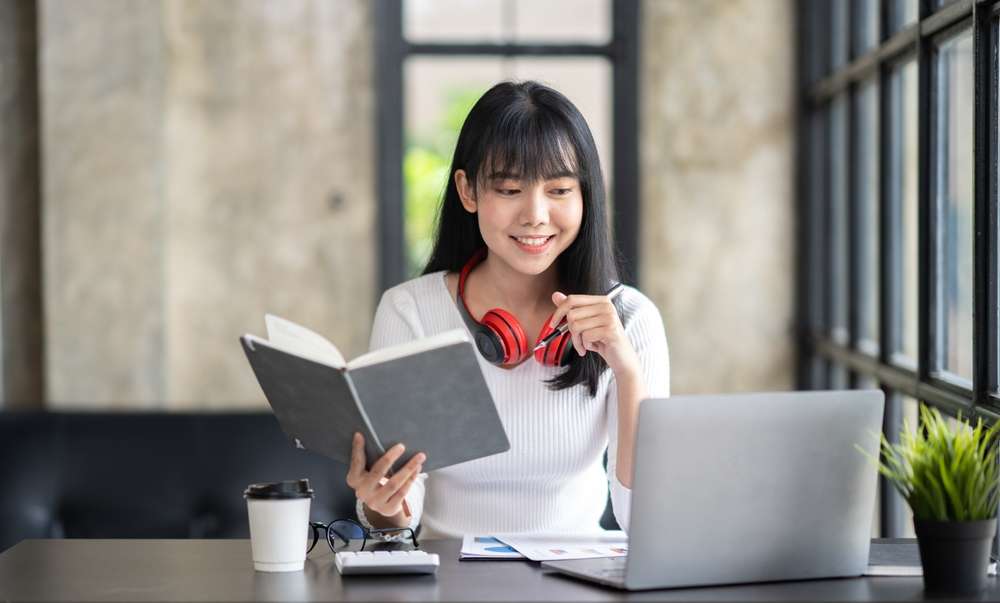中国の机に座りながら本を読んでいるアジア系の若い女性。