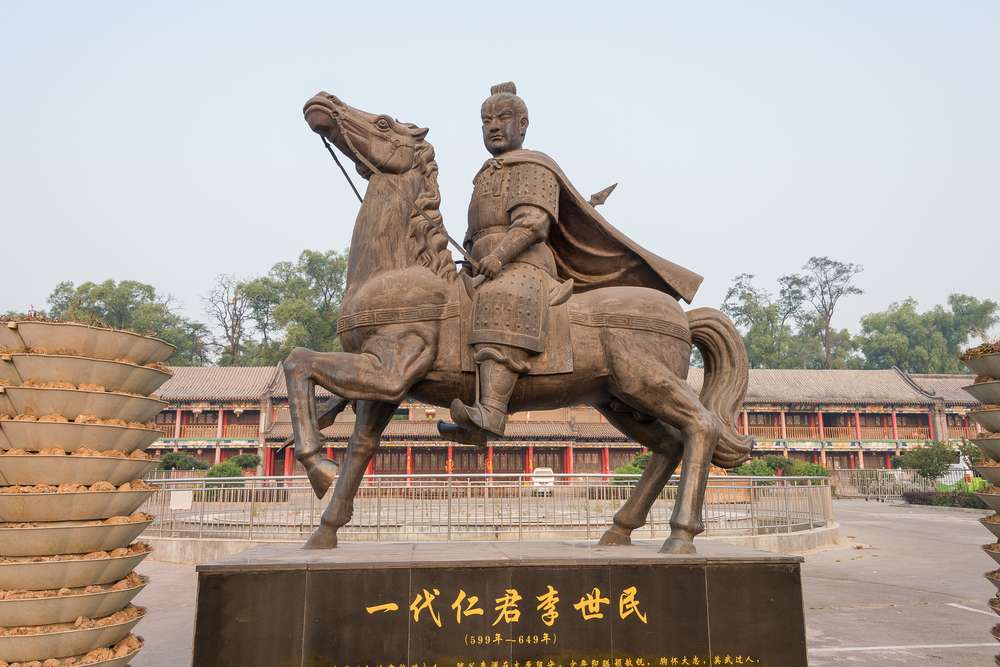 中国の建物の前にある馬に乗った男性の像。