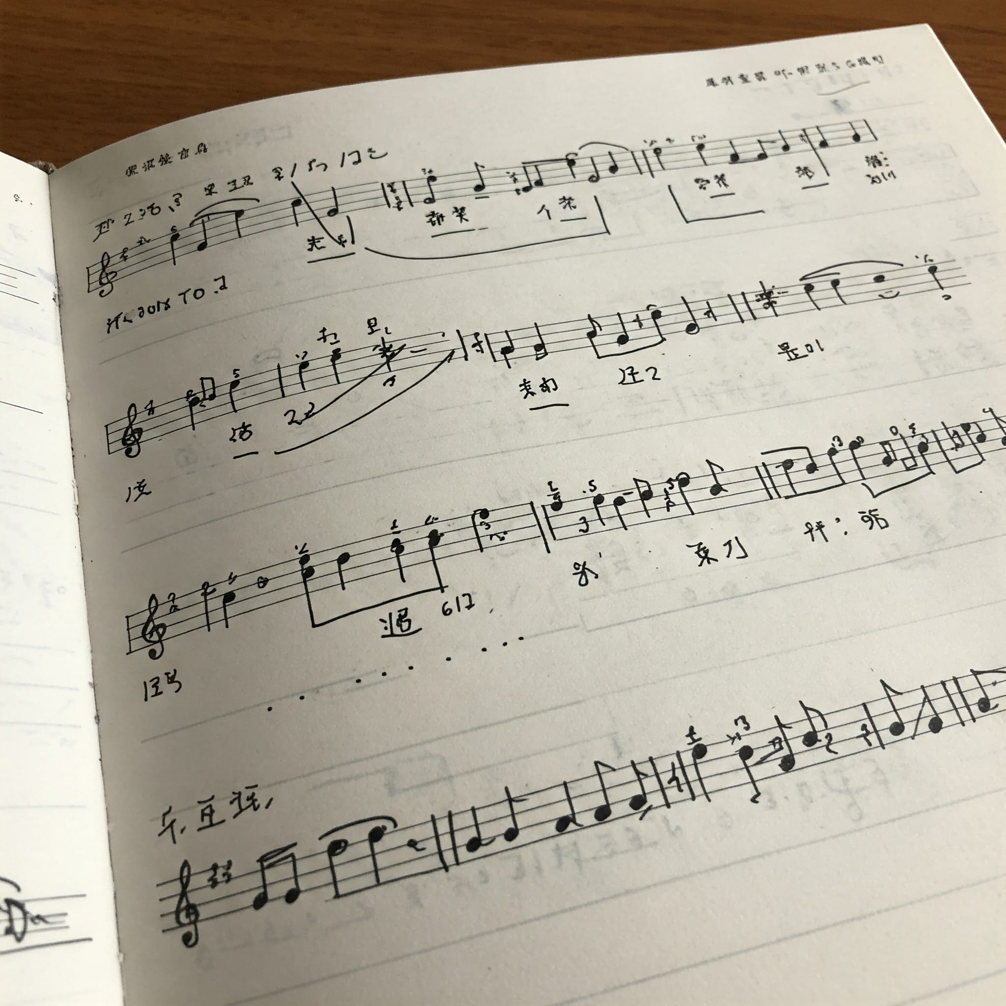 楽譜と中国語の歌詞が書かれたノートがあり、音符と声調記号が比較されている