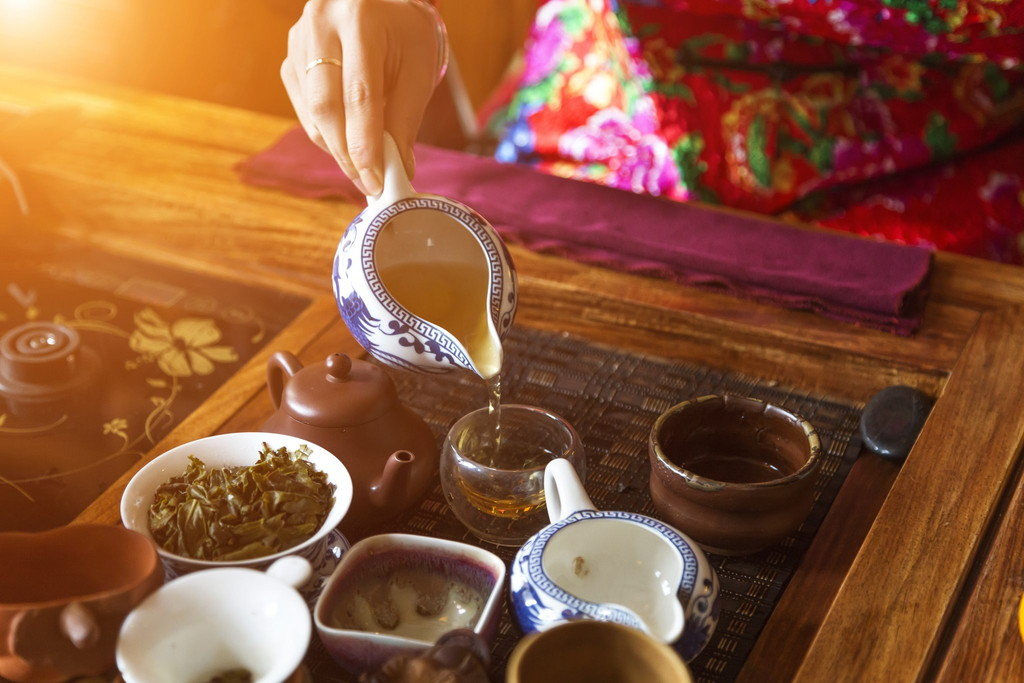 テーブルの上のカップにお茶を注ぐ中国の女性。