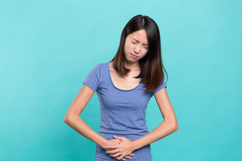 中国の青い背景にお腹を押さえるアジアの若い女性。