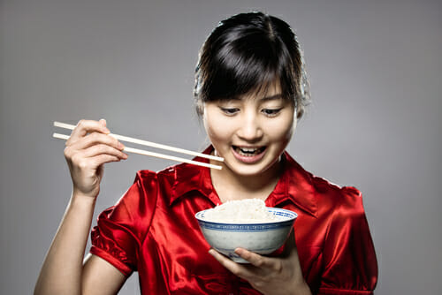 箸を持った若い女性がご飯茶碗を持っている。