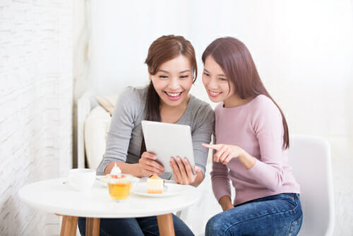 中国から来た 2 人のアジア人女性がテーブルに座ってタブレット コンピューターを見ています。