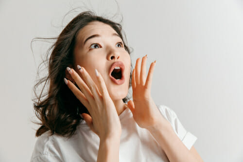アジア人の女性が顔に手を当てて驚く。