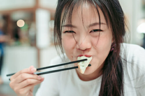 中国でお箸を使って寿司を食べる若いアジア人女性。