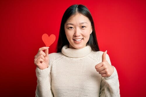 赤い背景にハートの形をした親指を示す若い中国人女性。