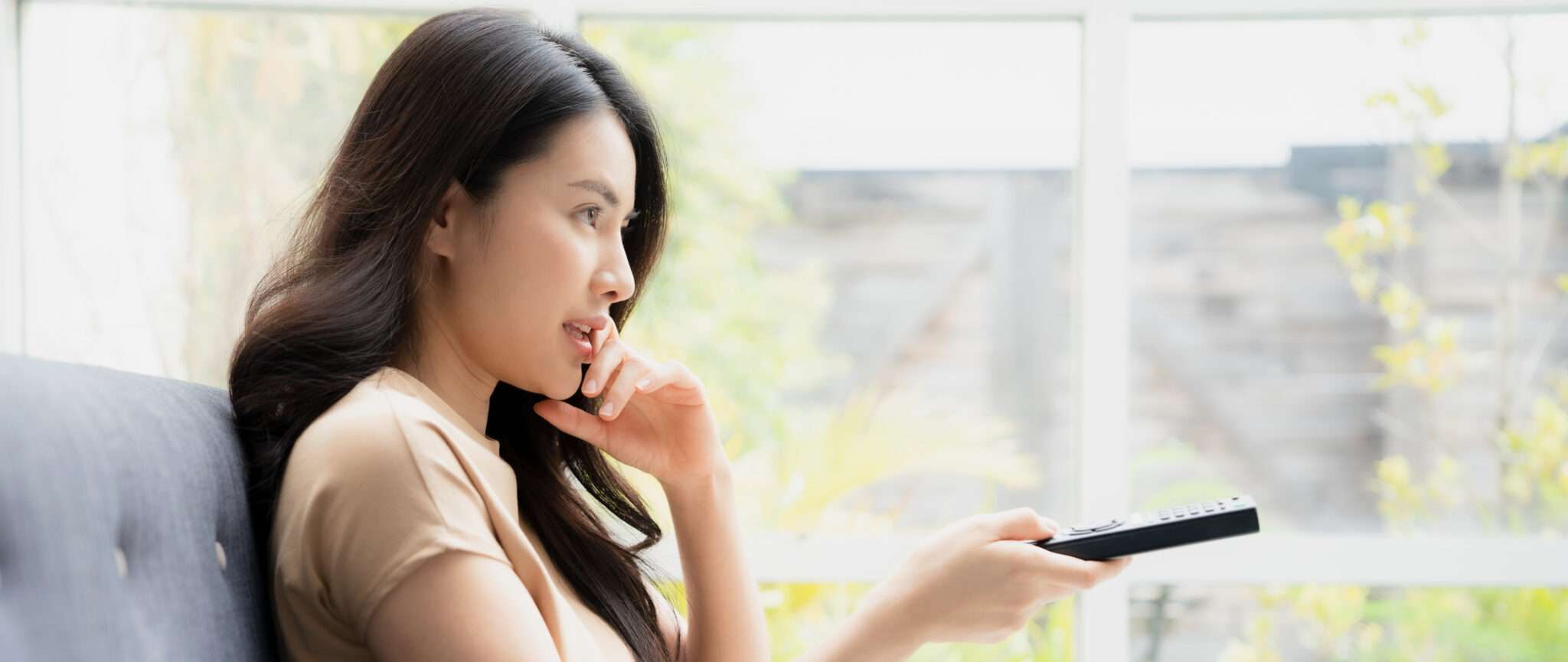中国の女性がソファに座ってリモコンを持っています。
