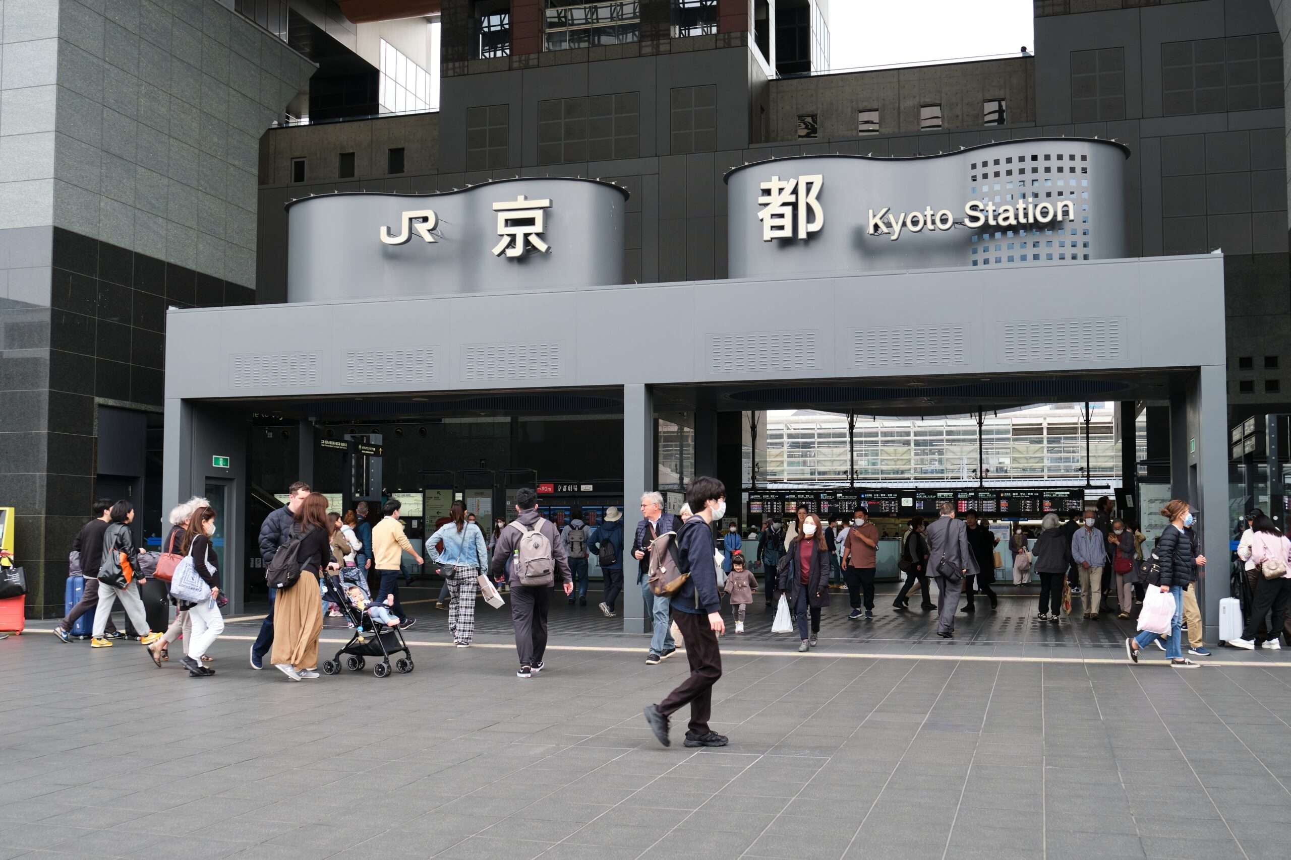日本の京都駅の外を歩く人々。言語レッスンを提供する中国語教室の近くで、日本語と英語の看板が見える。