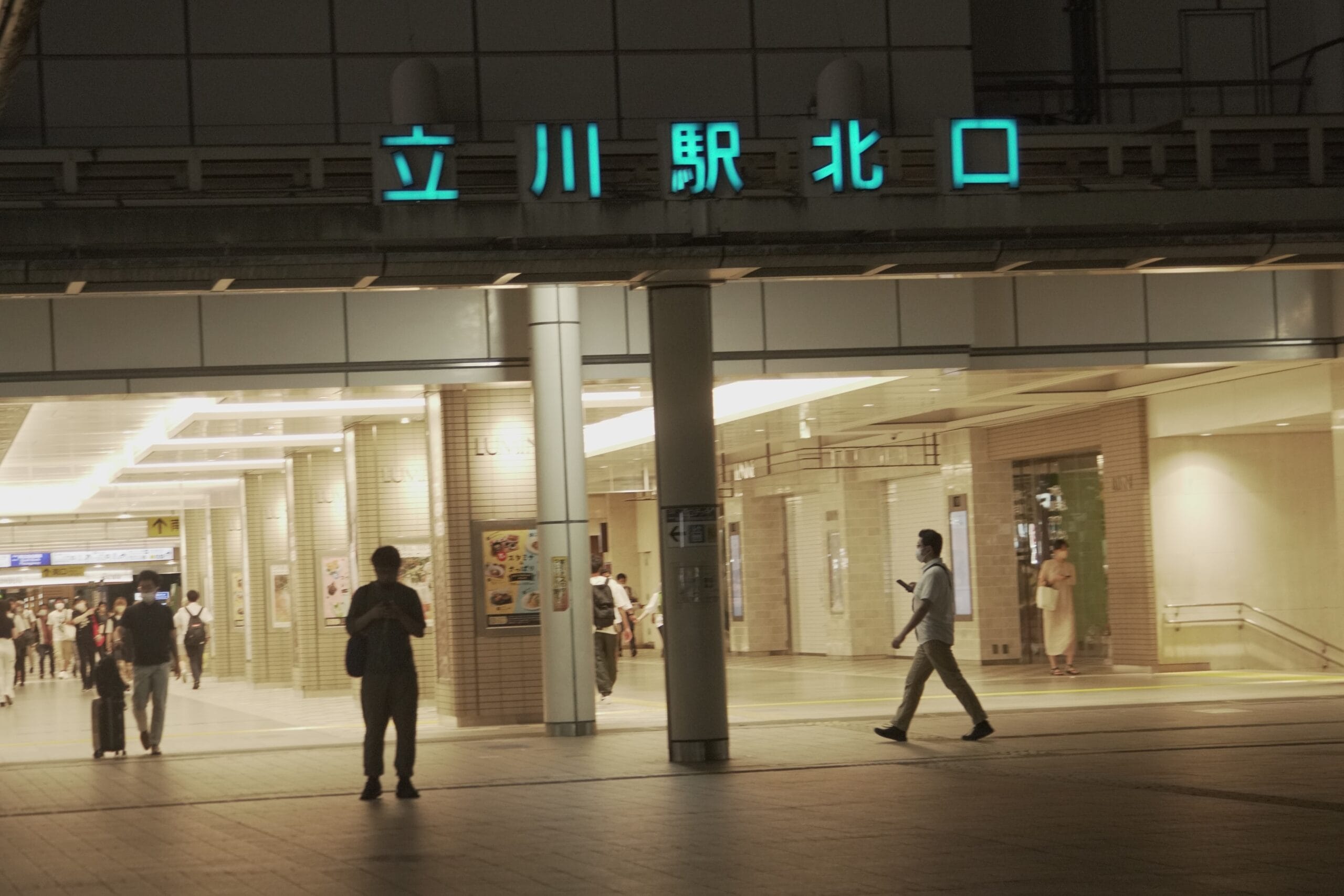 夜、立川駅北口近くの中国語教室の前を通り過ぎる人々。.