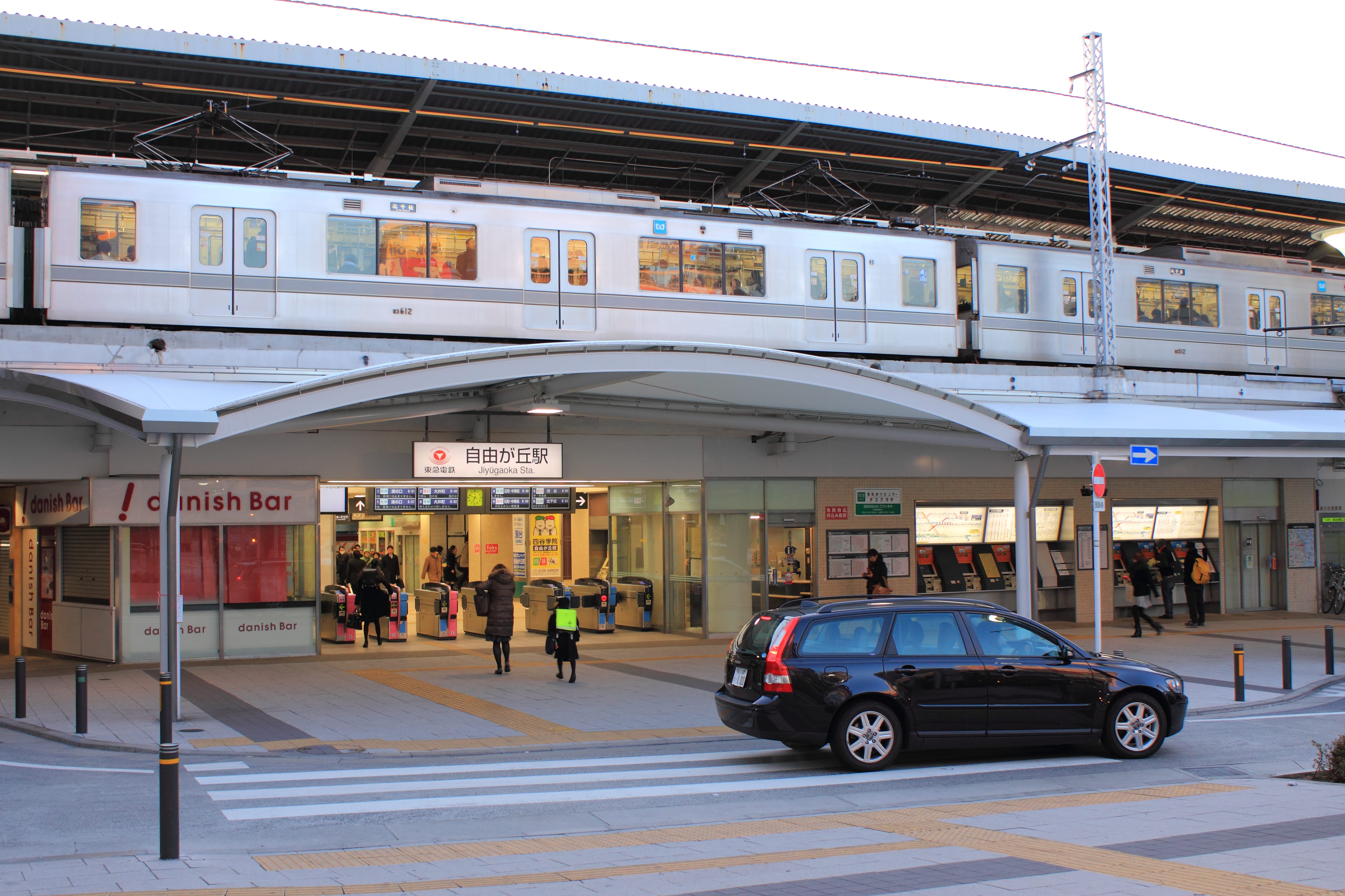 駅の出入り口の上の高架に電車が停車し、下に人が出入りしている。.