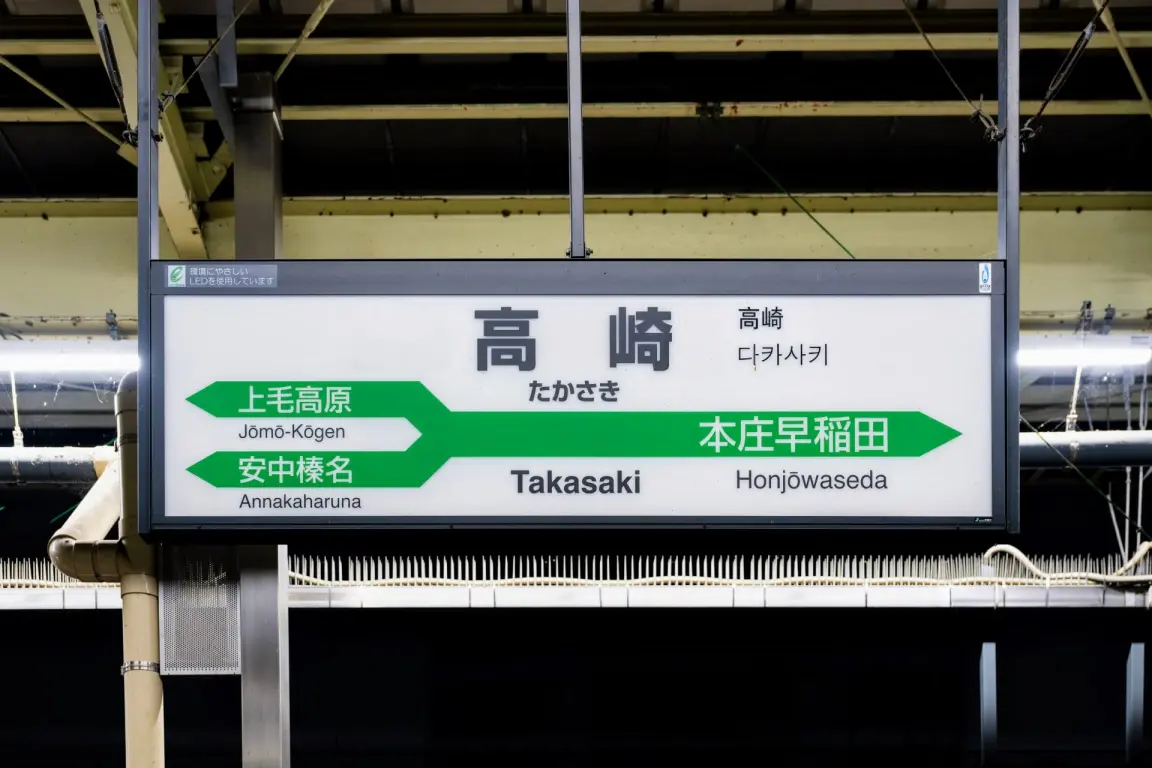 日本語、英語、韓国語で常総高原、安中春名、本庄早稲田方面への道順を表示する高崎の駅看板。.