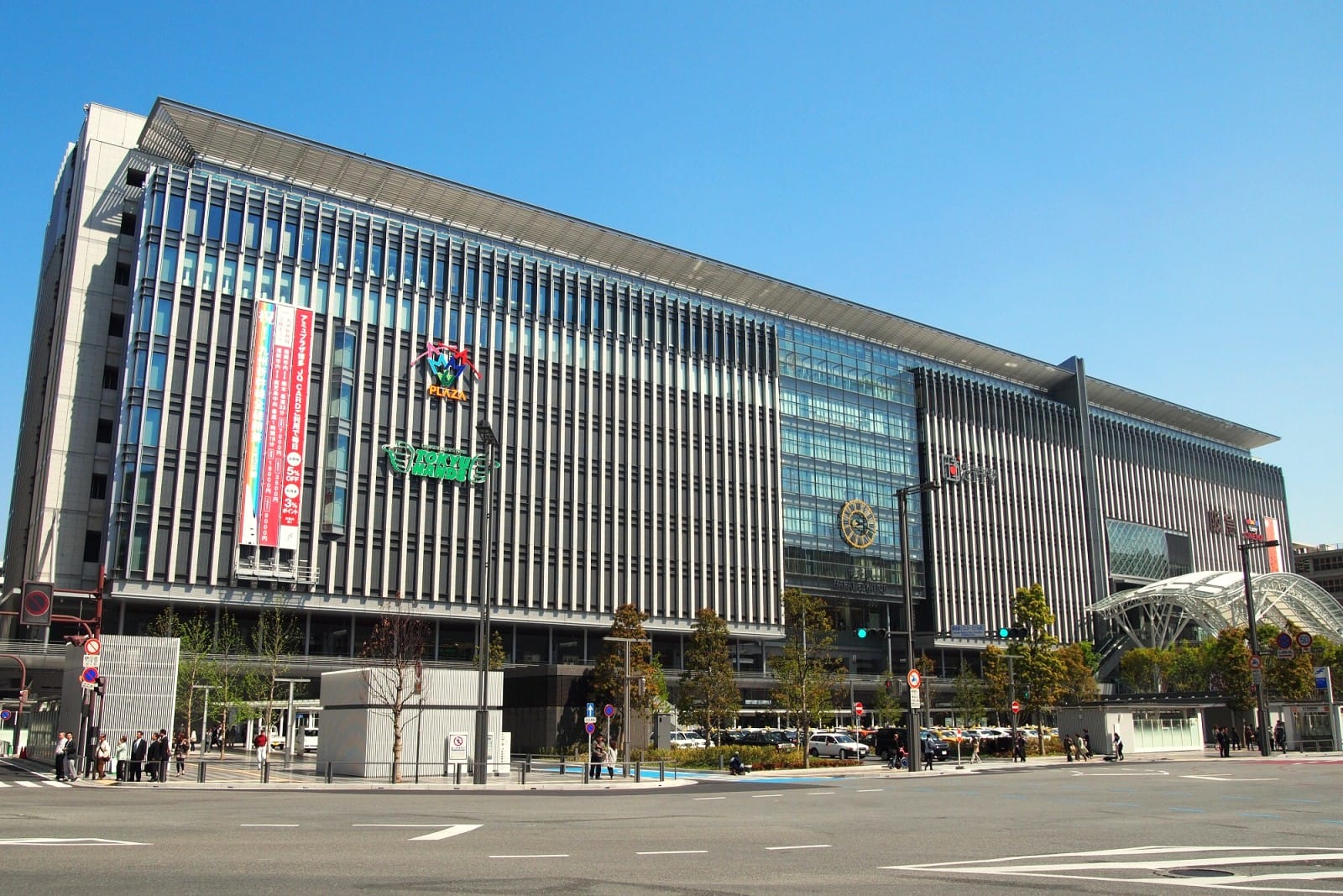 ガラスと金属製のファサードを持つ大きな近代的な建物で、複数の看板やバナーが掲げられている。.