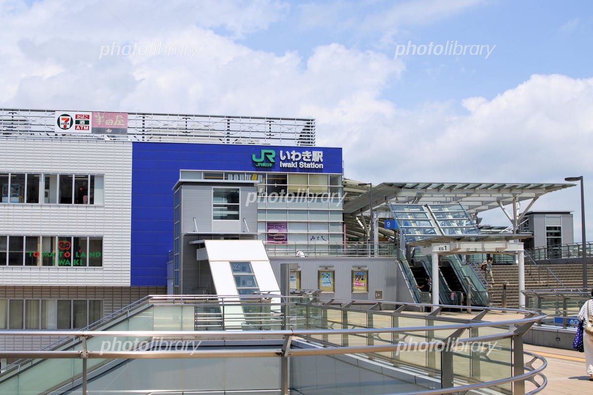 日本のいわき駅の外観。青と白の駅舎にJRの看板、ガラスの手すり、入口へと続くエスカレーターがある。.