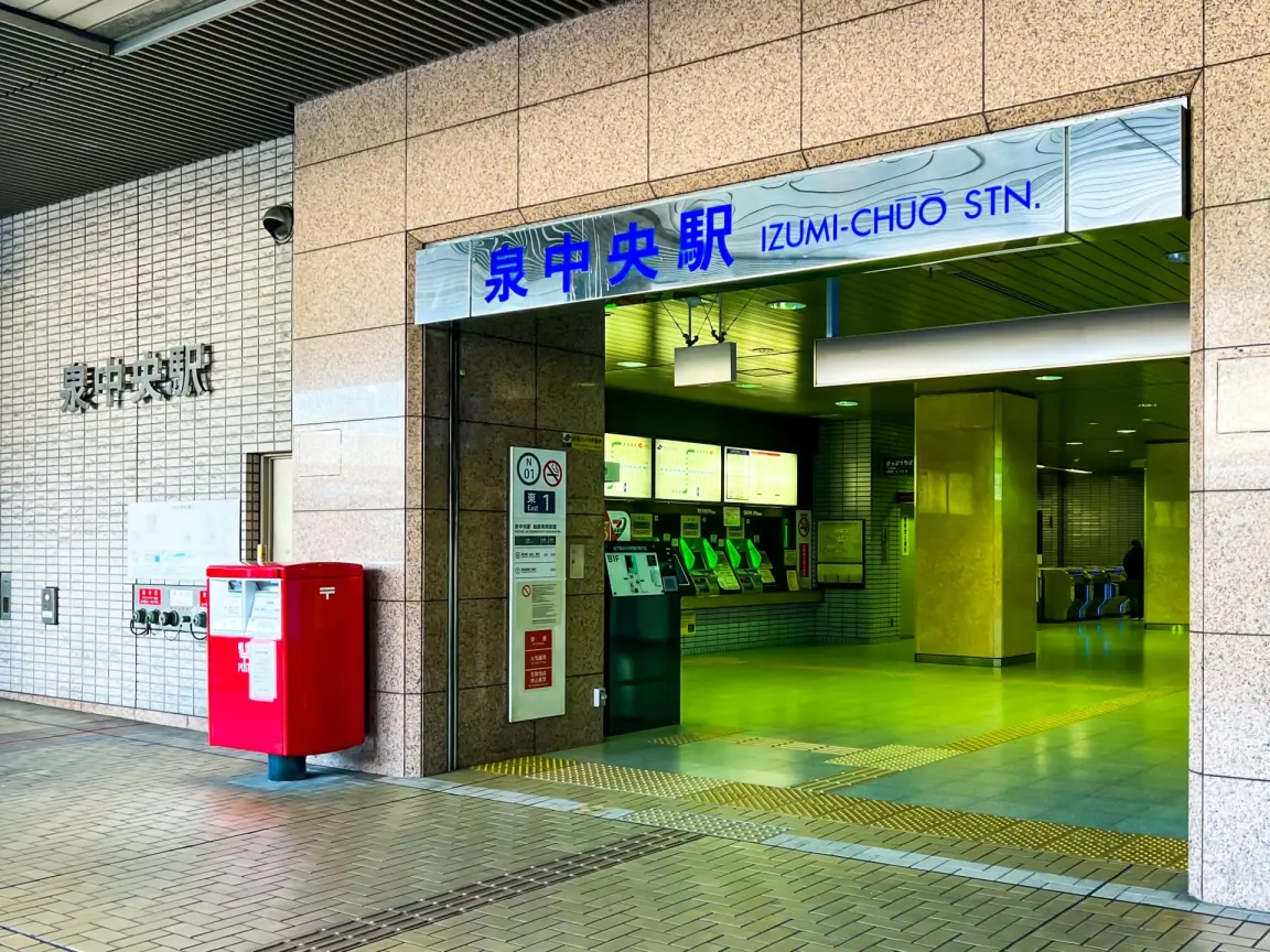 和泉中央駅入口。駅構内に券売機、その上に看板、出入り口付近に赤いポストと案内板がある。.