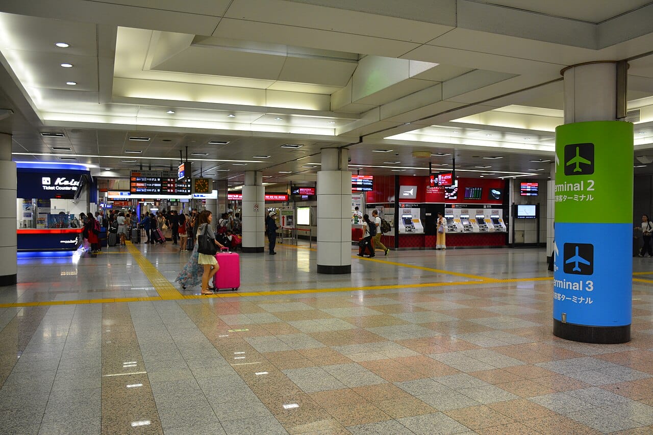 乗客は、券売機、案内板、第2ターミナルと第3ターミナルへの案内板がある、広々として明るい駅構内を歩く。.