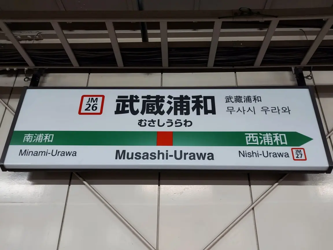 南浦和（JM25）、西浦和（JM27）への行き方を示す、日本語、ローマ字、ハングルで書かれた武蔵浦和の駅名標。.