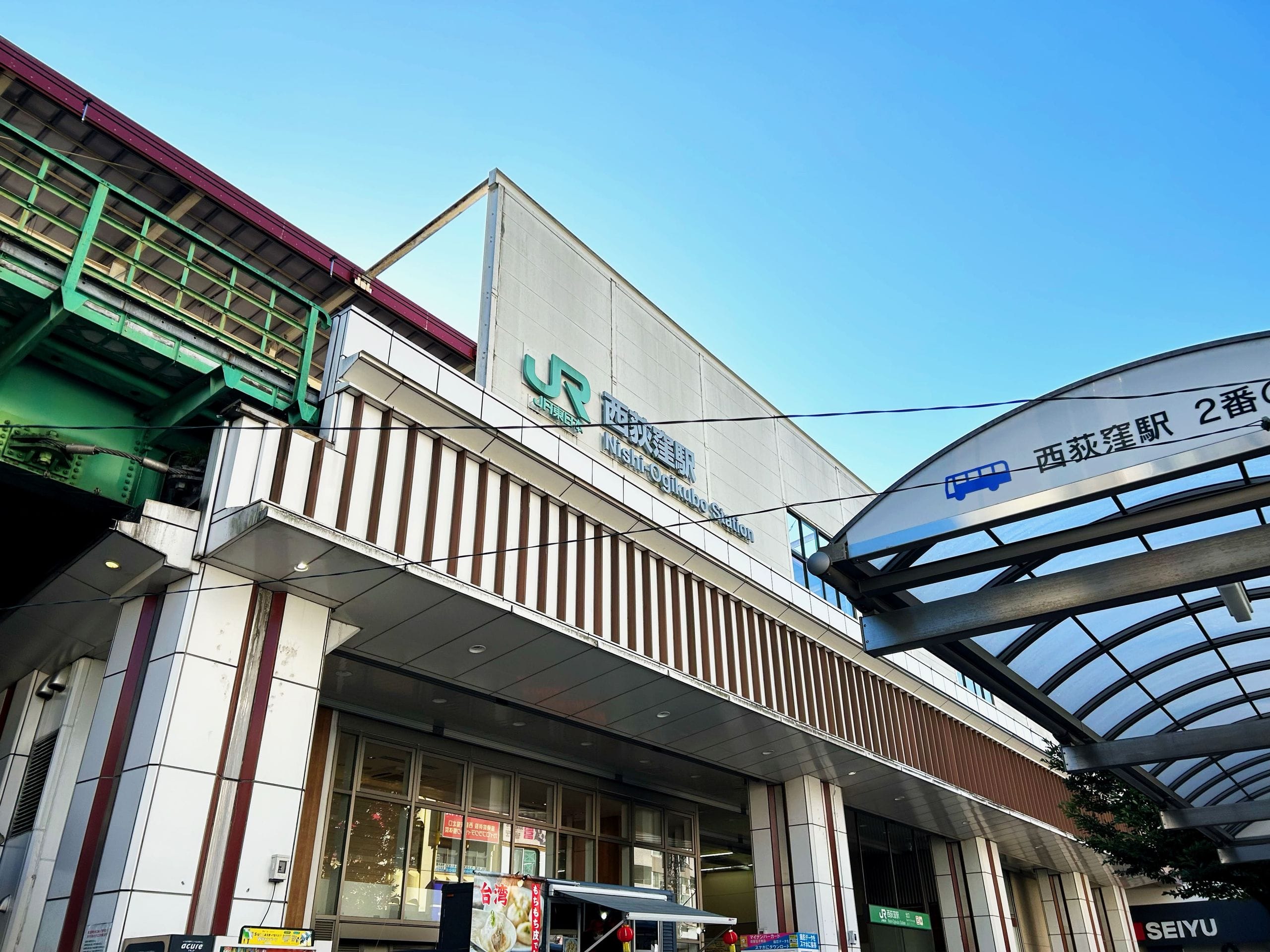 快晴の青空の下、駅の看板と屋根付き通路の一部が見える。.