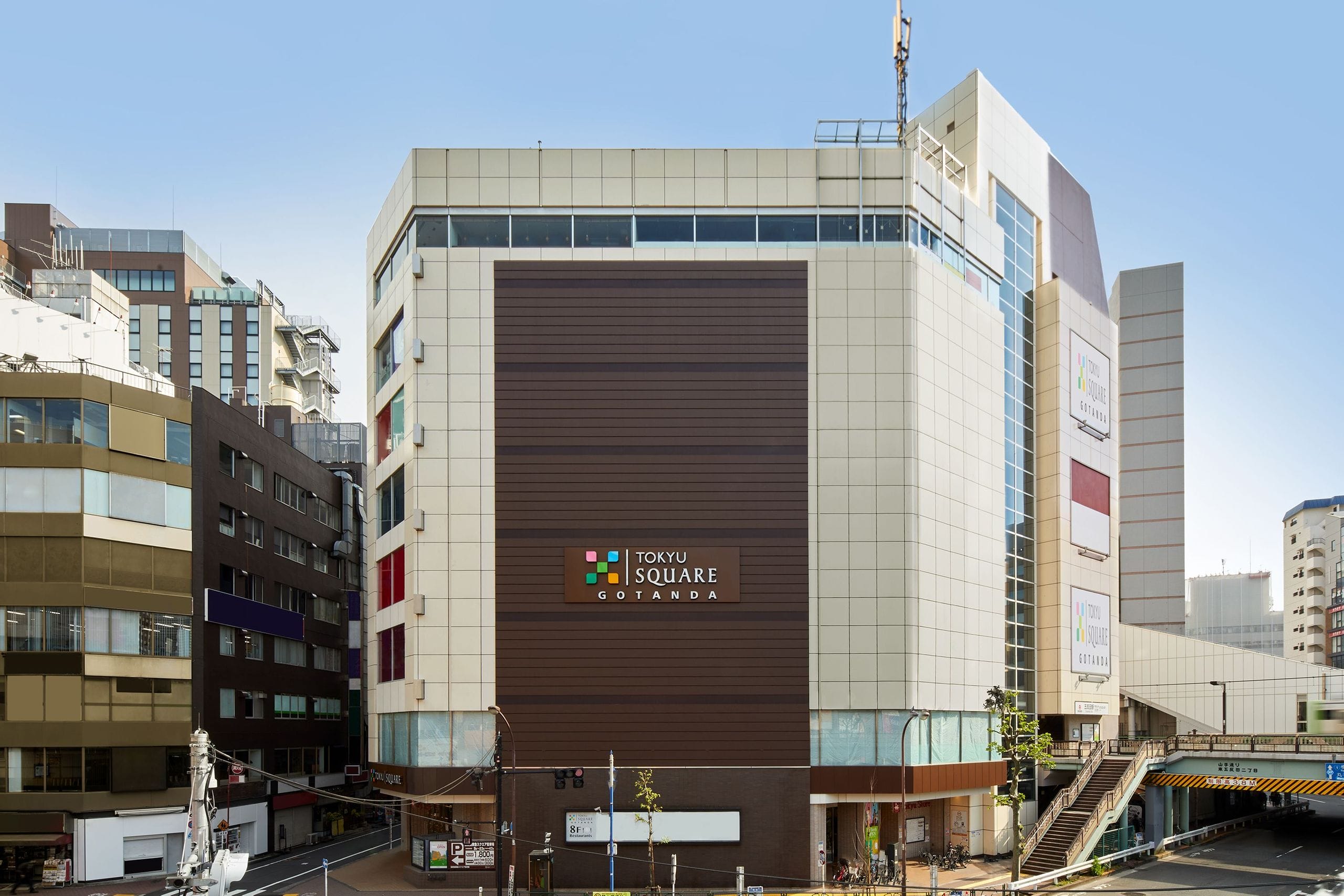 ファサードに「東急スクエア五反田」の看板が掲げられた、近代的な大型ビルで、周囲には他の都市型のビルが立ち並び、右側には歩行者用通路がある。.
