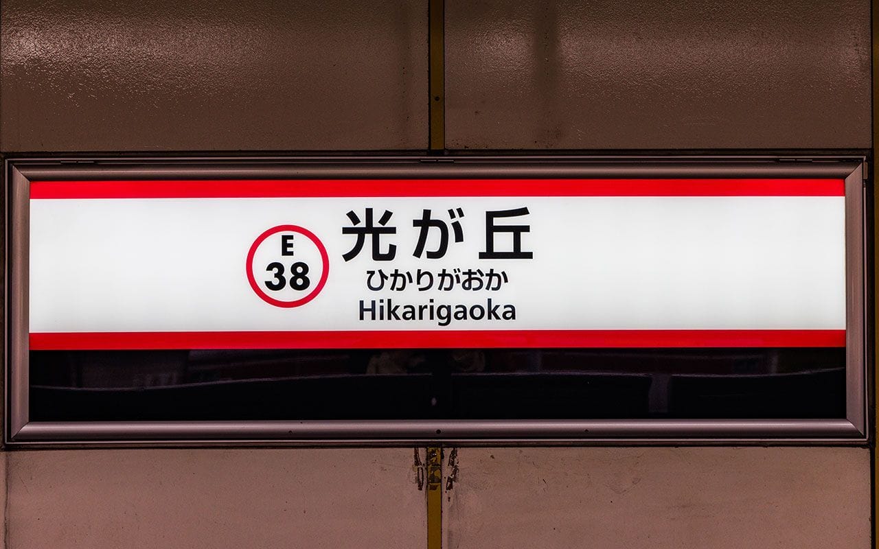 地下鉄駅の看板で、白地に赤のアクセントが入り、日本語と英語で「ヒカリガオカ」と表記され、駅コードはE-38となっている。.