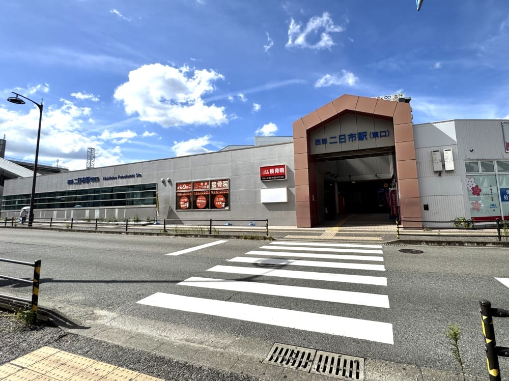 青空に雲が点在する中、西宮駅の西口と、その前にある横断歩道の風景。.