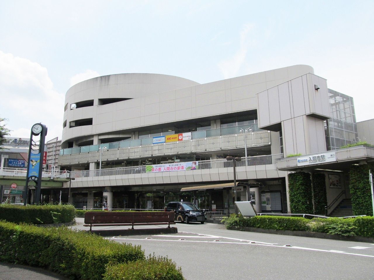 ガラス製の手すりが施された、モダンな白い高層ビルで、1階には店舗が入っており、タクシーや緑地のある駐車場の隣に位置している。.